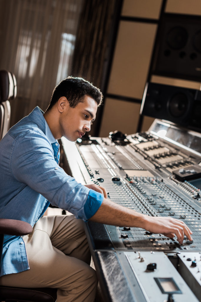 Mixed race sound producer working at mixing console in recording studio