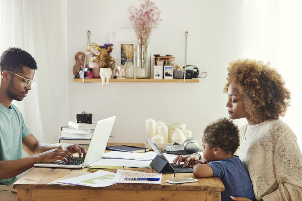 Young man working on laptop. Woman is using digital tablet while sitting with son at table. They are in kitchen at home.