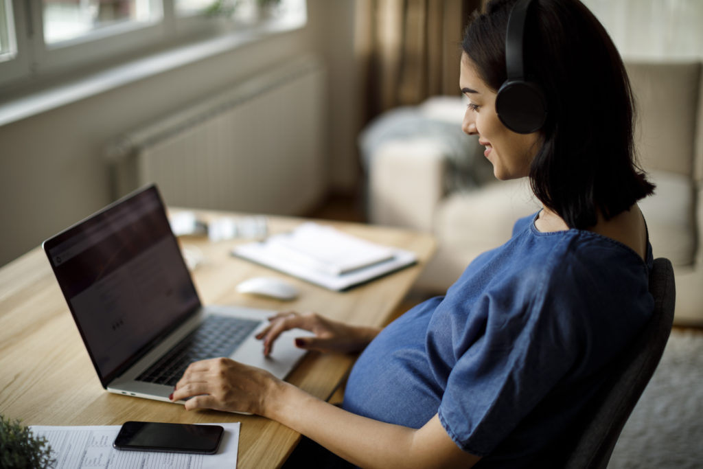 Pregnant woman with headphones using laptop