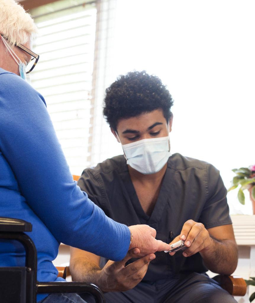 African-American male medical employee wearing gray scrubs and face mask interacts with a senior aged patient