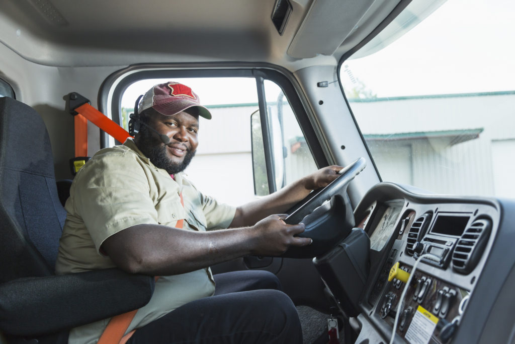 African-American male truck driver looking at the camera as he sits in the driver's seat wearing his seat belt