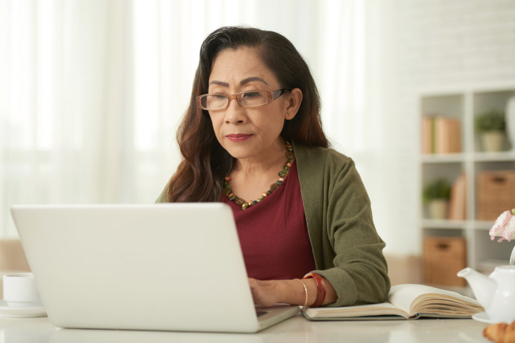 Mature woman in eyeglasses using laptop at the table at home