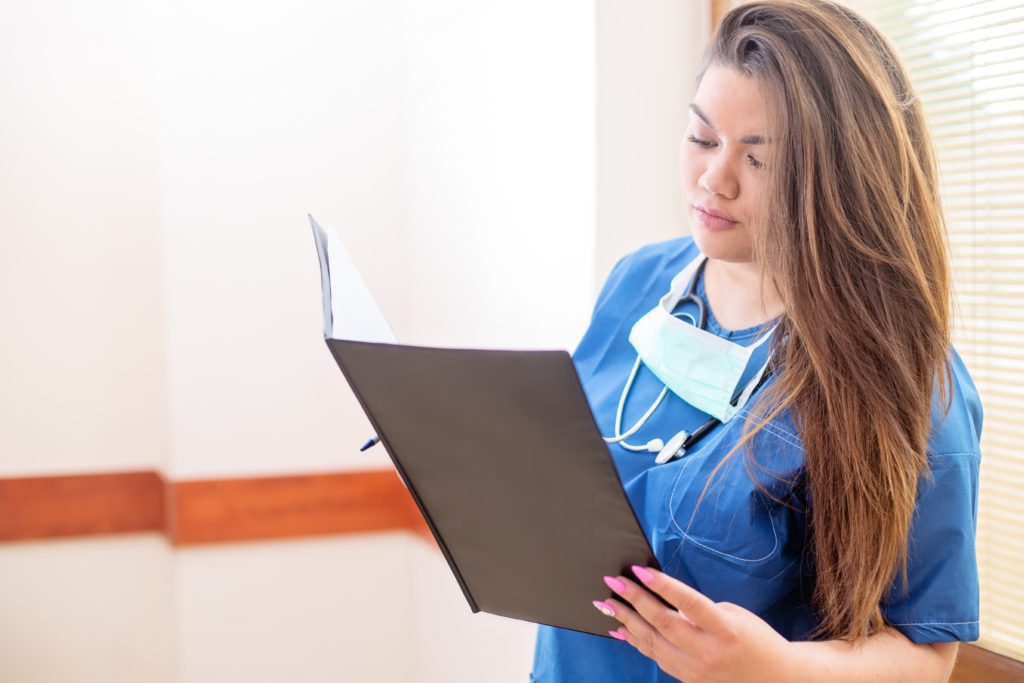 Close-up photo of young female medical professional reading a medical report in a hospital hallway, wearing blue uniform