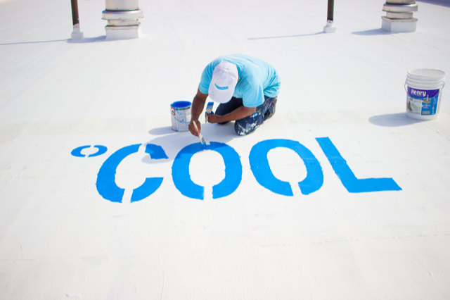 person painting roof white with the word COOL painted in blue