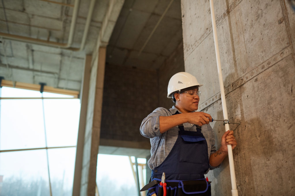 Wide angle portrait of female worker wearing hardhat and setting up pipes while working on construction site, copy space