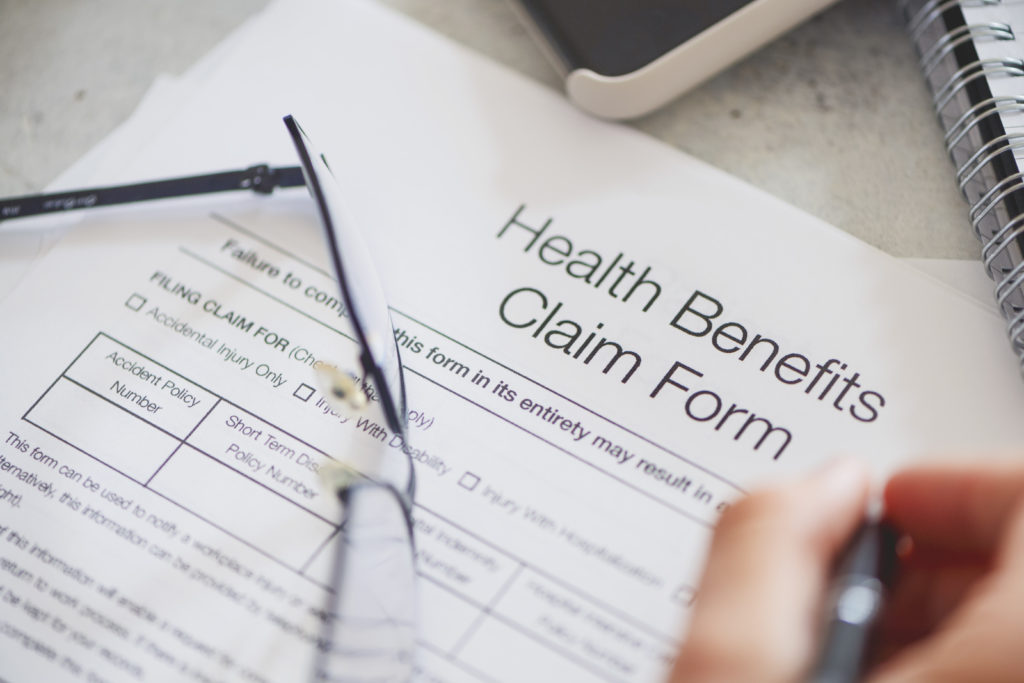 Person filling in a health benefits application form. There are also a pair of glasses on the table