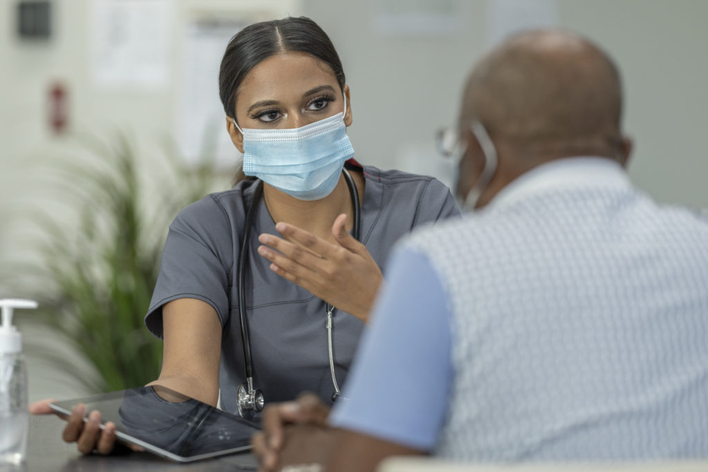 A senior patient and a female doctor meet in a medical clinic while wearing protective face masks to avoid the transfer of germs.